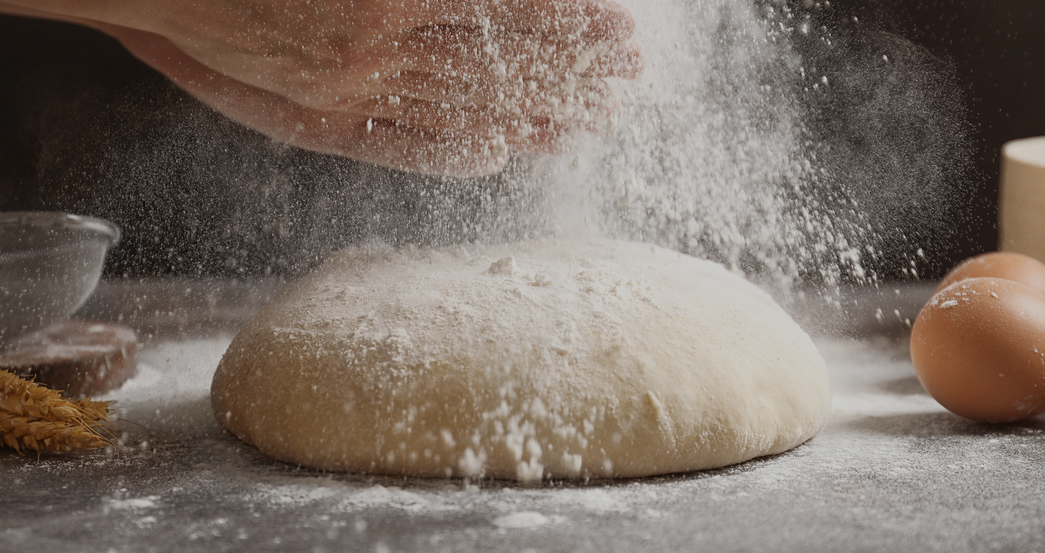 Des mains qui saupoudre de la farine sur une boule de pâte à pain.