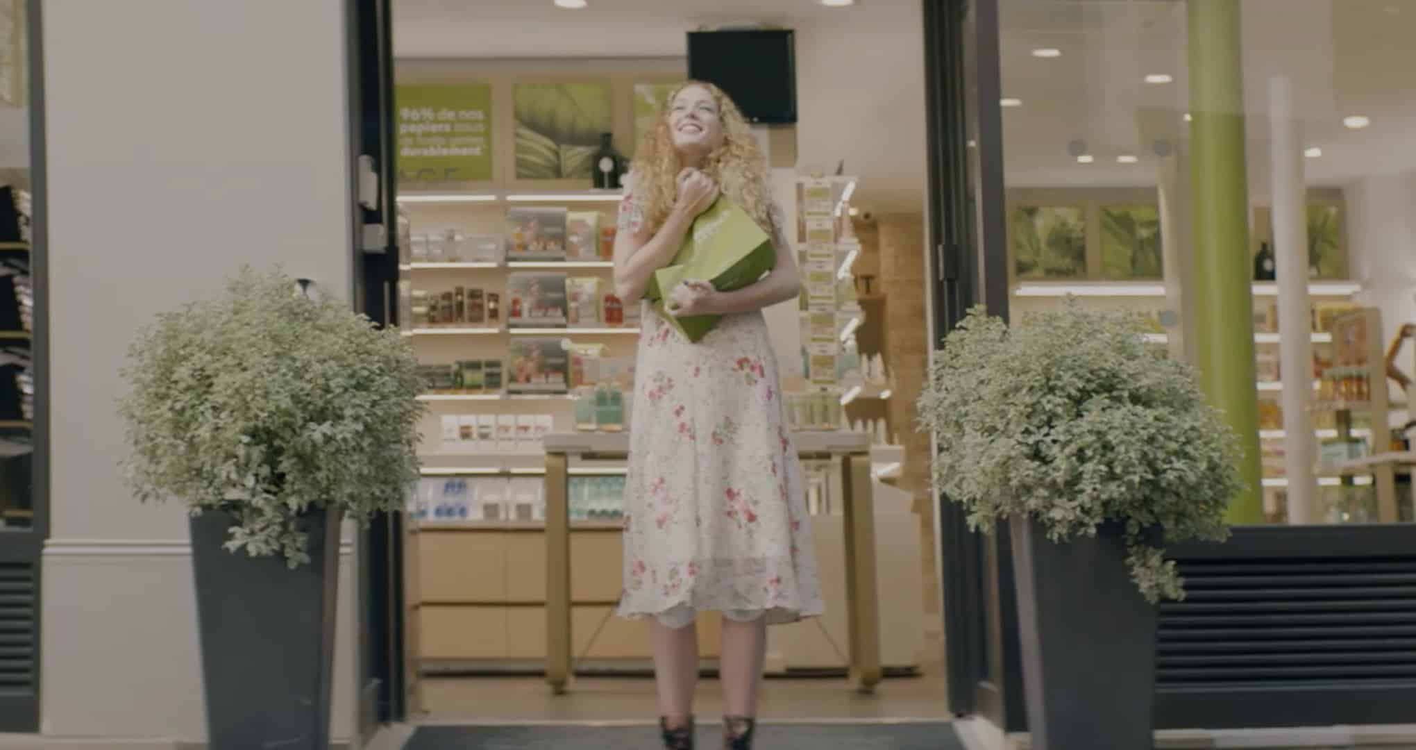 Une femme sort d’une boutique Yves rocher et sert un sac en carton de l’enseigne dans ses bras